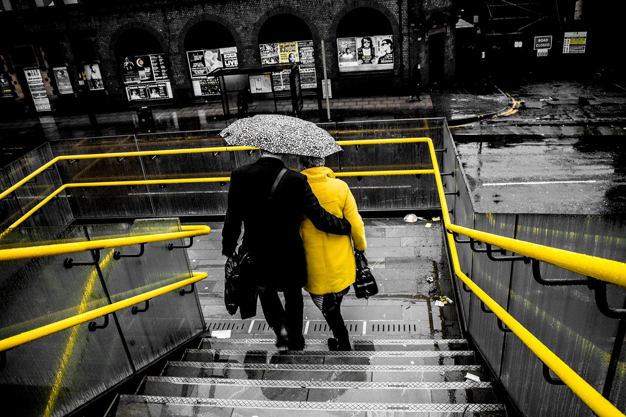 A couple walks down city stairs under an umbrella on a rainy day.